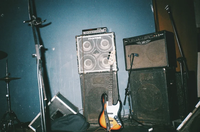 A vintage electric bass guitar stands against music amplifiers in a studio setting — an editorial image for "How the British Invasion Transformed Popular Music."