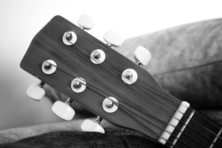 Monochrome close-up of an acoustic guitar headstock with tuning pegs — an editorial image for "The Folk Revival and the Rise of the Singer-Songwriter."