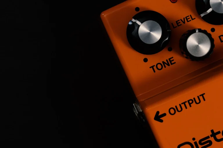 Detailed close-up of an orange guitar distortion pedal showcasing tone and level knobs — an editorial image for "How Grunge Changed Rock Music in the 1990s."