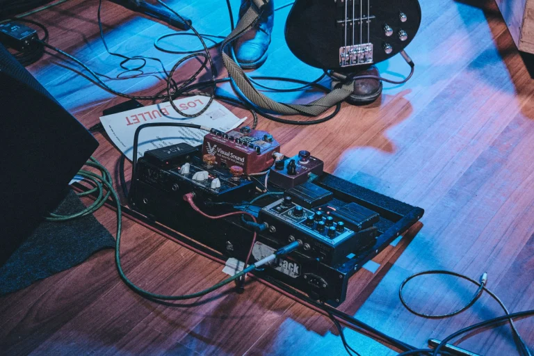 Close-up of a guitar pedal board on stage floor with a bass guitar and cables — an editorial image for "The Origins and Evolution of Heavy Metal."